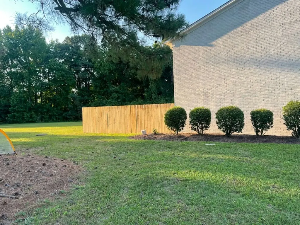 Wood privacy fence beside shrubs and a brick building in Hampton, VA