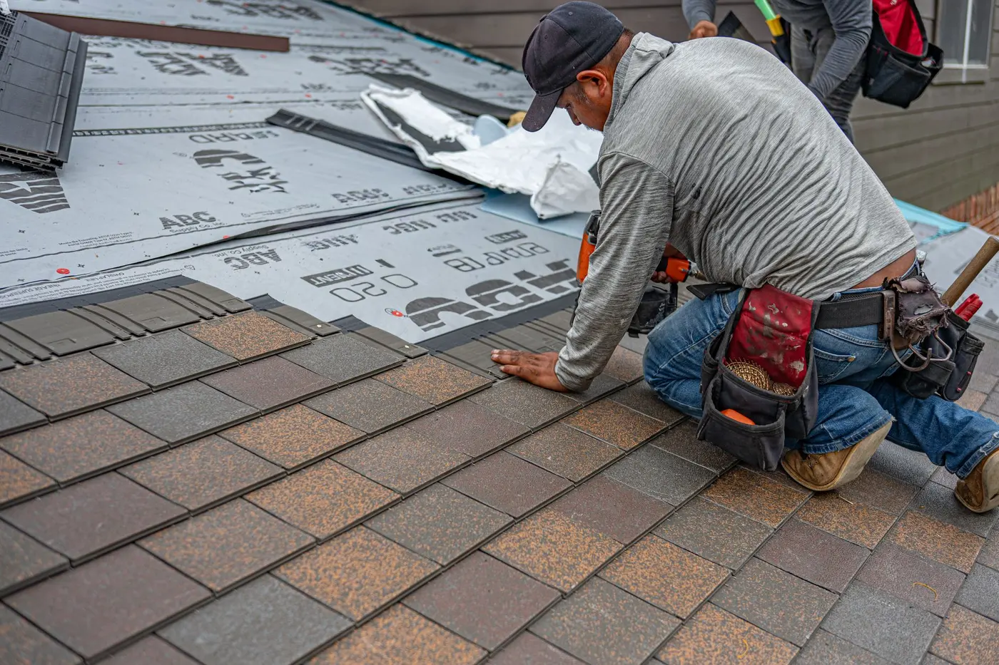 Roofer kneeling on asphalt shingles during roofing work in Hampton, VA